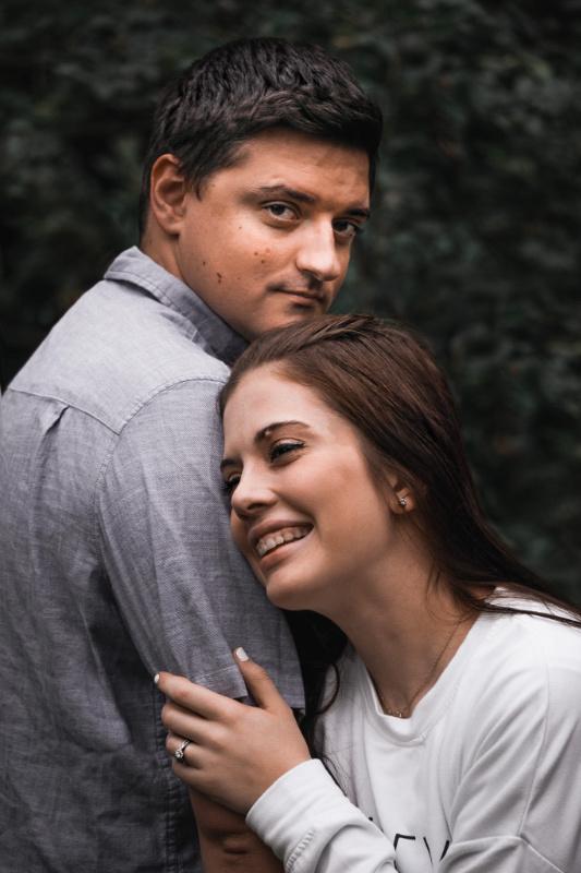 Couple embracing against a dark, leafy backdrop in a moody, low-key style