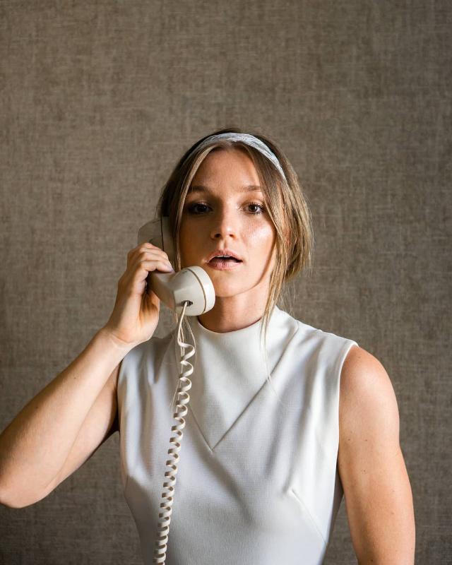 Model in a sleeveless cream top holding a vintage telephone against a linen backdrop