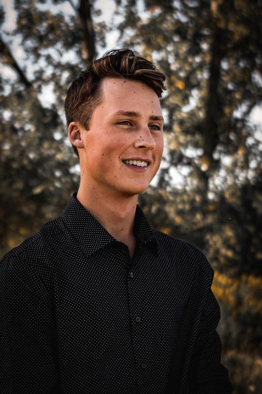 Smiling high-school senior photographed outdoors against golden, backlit trees