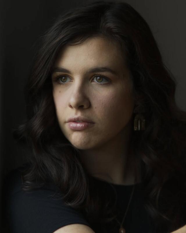 Moody, low-key studio portrait of a woman lit softly against a dark backdrop